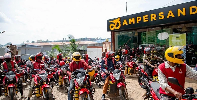 Lots of Ampersand e-motorcycle users gathered infront of an Ampersand-branded building. 