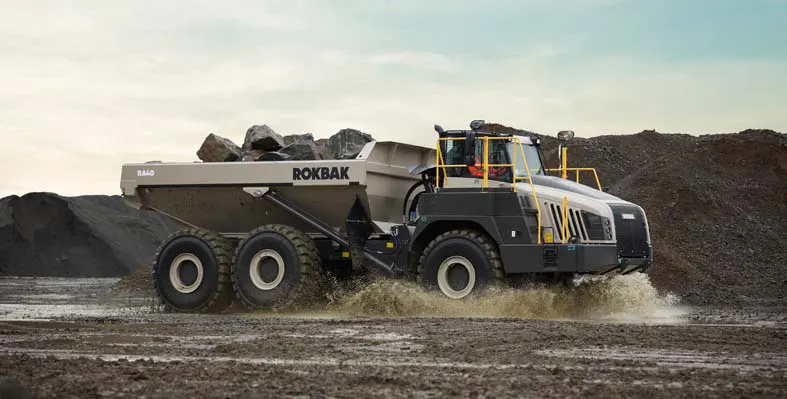 A Rokbak RA40 driving quickly through a puddle, carrying rocks. 