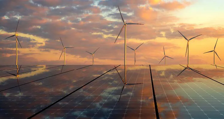 An image depicting solar panels in the foreground with wind turbines behind. 