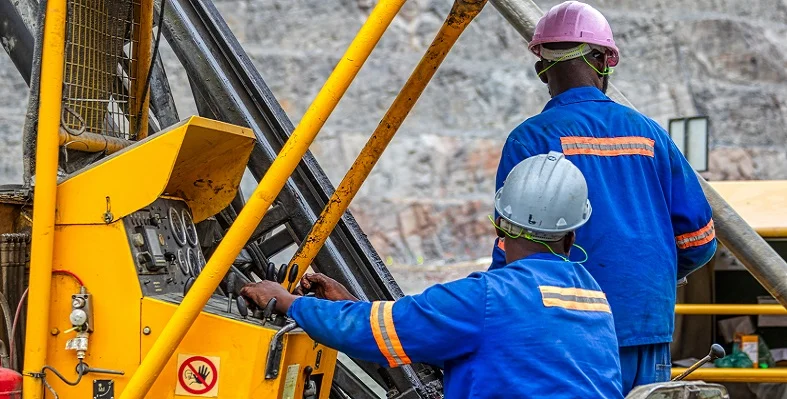 Two mine workers operating a piece of equipment on a mine site. 