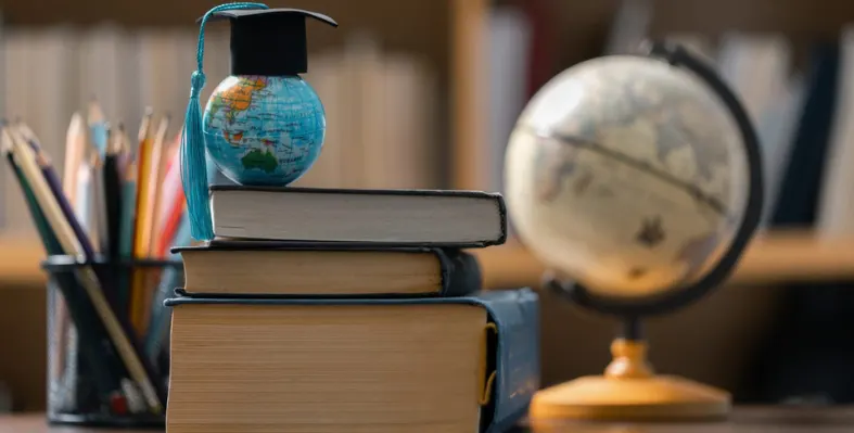 A globe with a top hat on top of a pile of books.