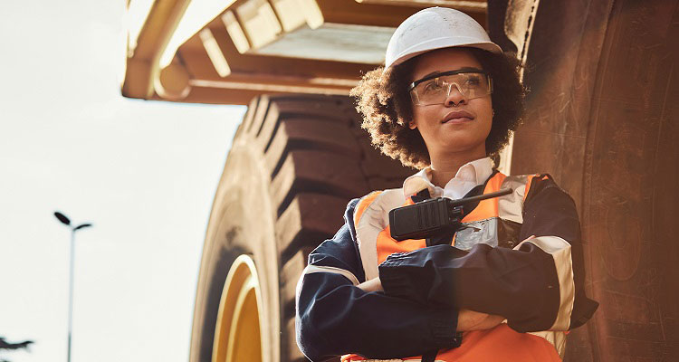 A female miner standing in front of a dump truck. 