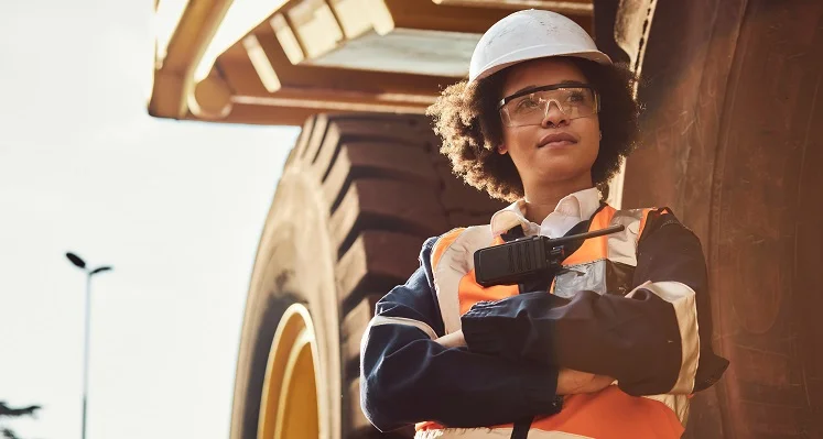 A women miner standing in front of a large piece of machinery. 