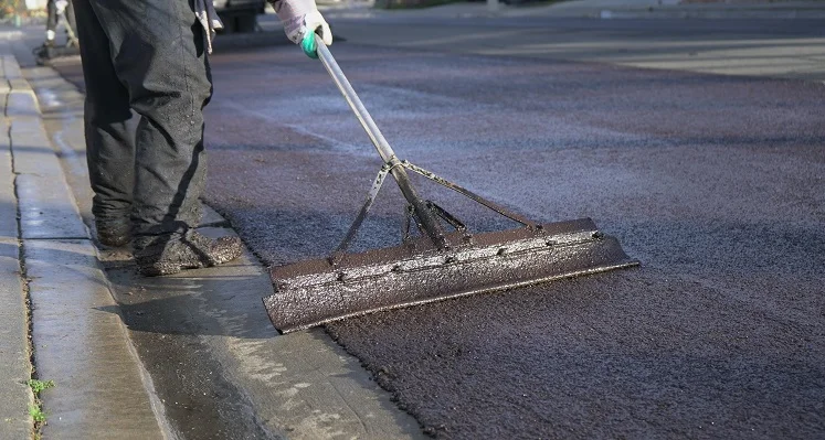 A worker laying fresh slurry seal on a road. 