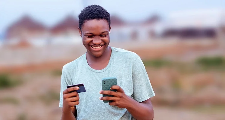 An African man looking at his phone and credit card.