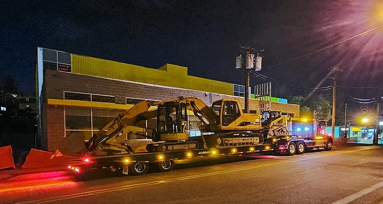 A travelling axle unit carrying construction equipment through a street.